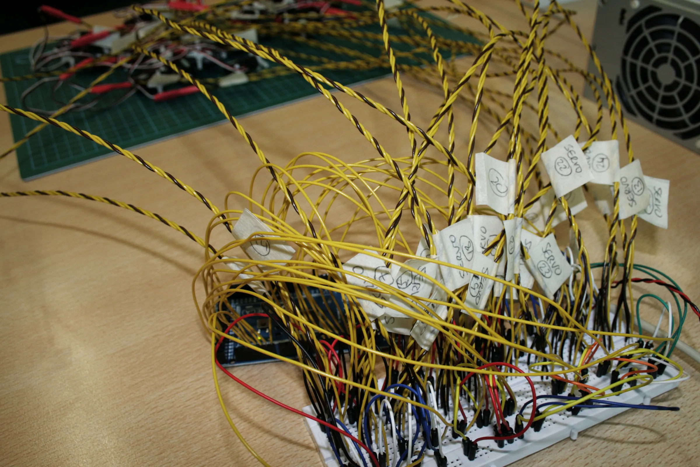 A tangle of labelled yellow servo leads running into a breadboard and Arduino beside a power supply
