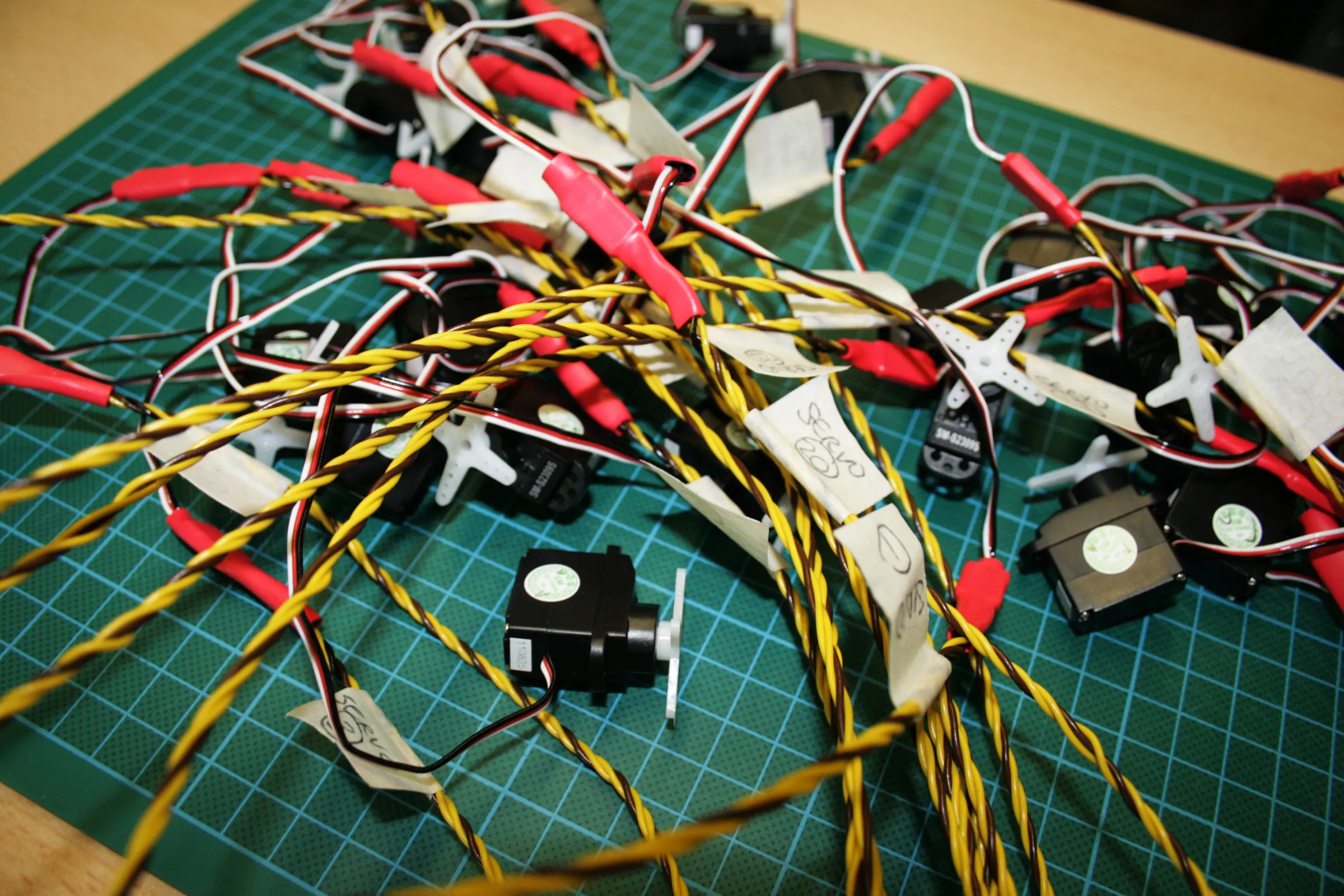 Servos on a cutting mat with twisted yellow and black leads, each marked with a numbered tape label
