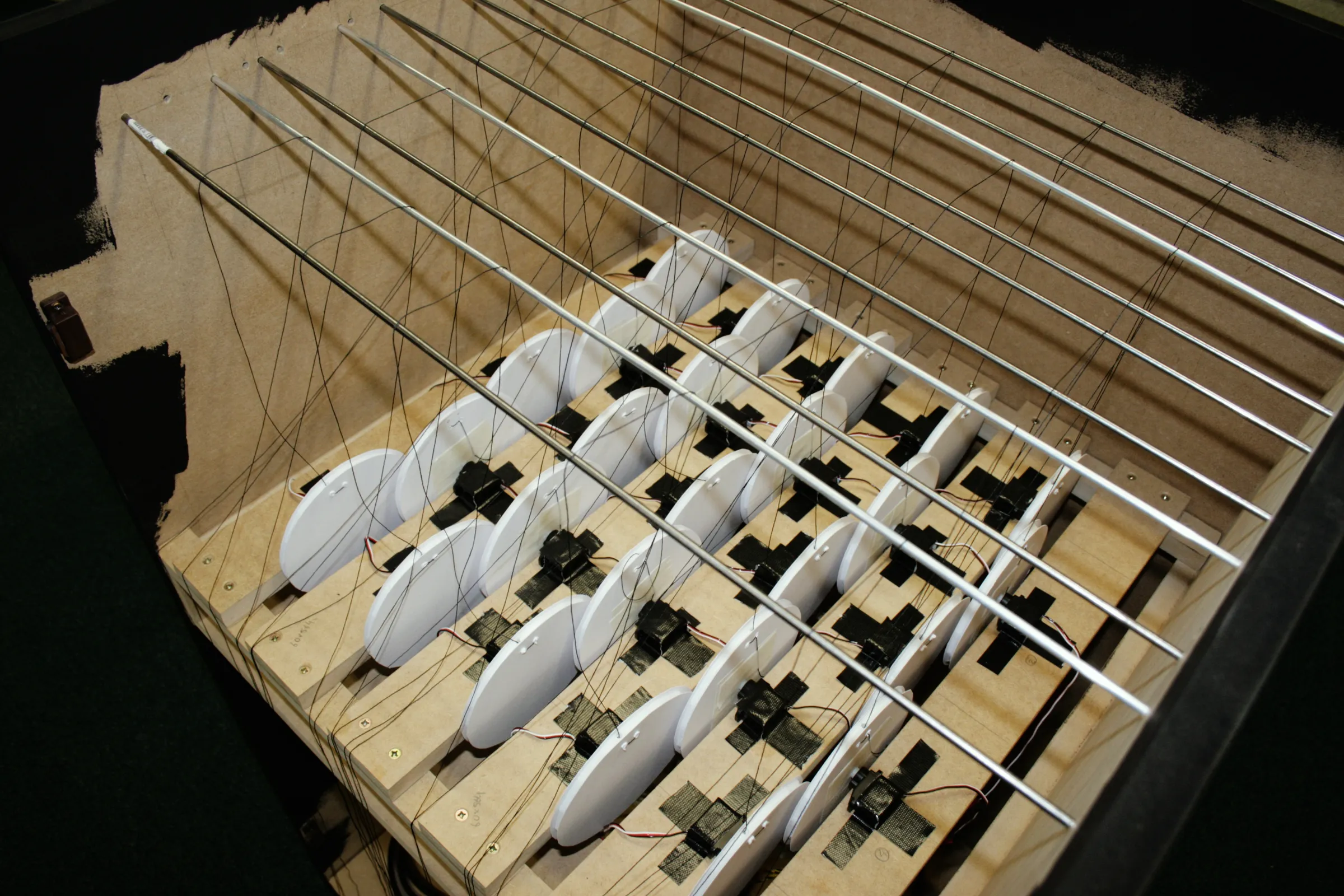 View into the top of the cabinet showing rows of white discs on servos, with threads running up to parallel metal guide rods