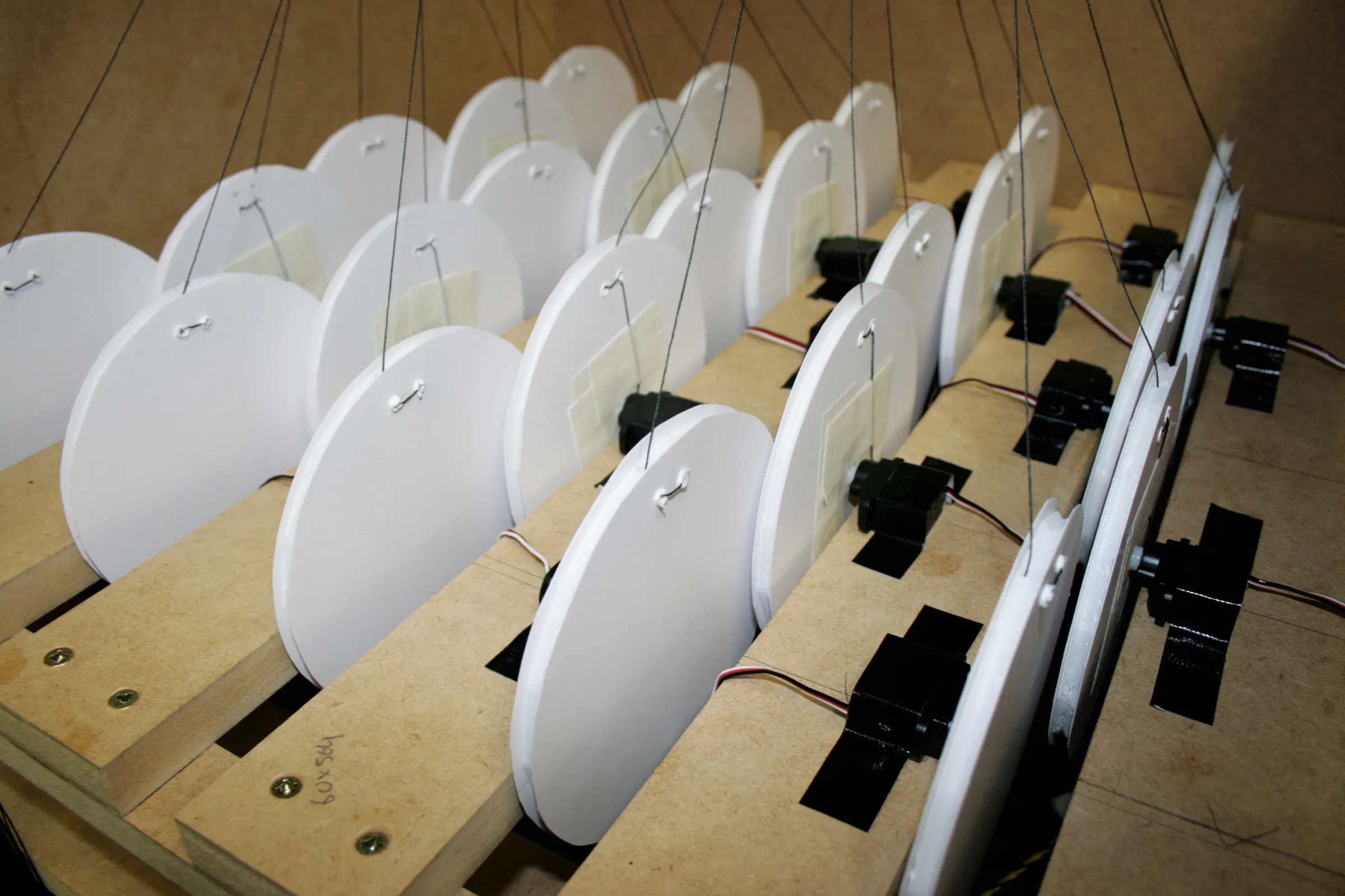 Close-up of white discs mounted on black servos in slotted wooden shelves, with threads leading upward