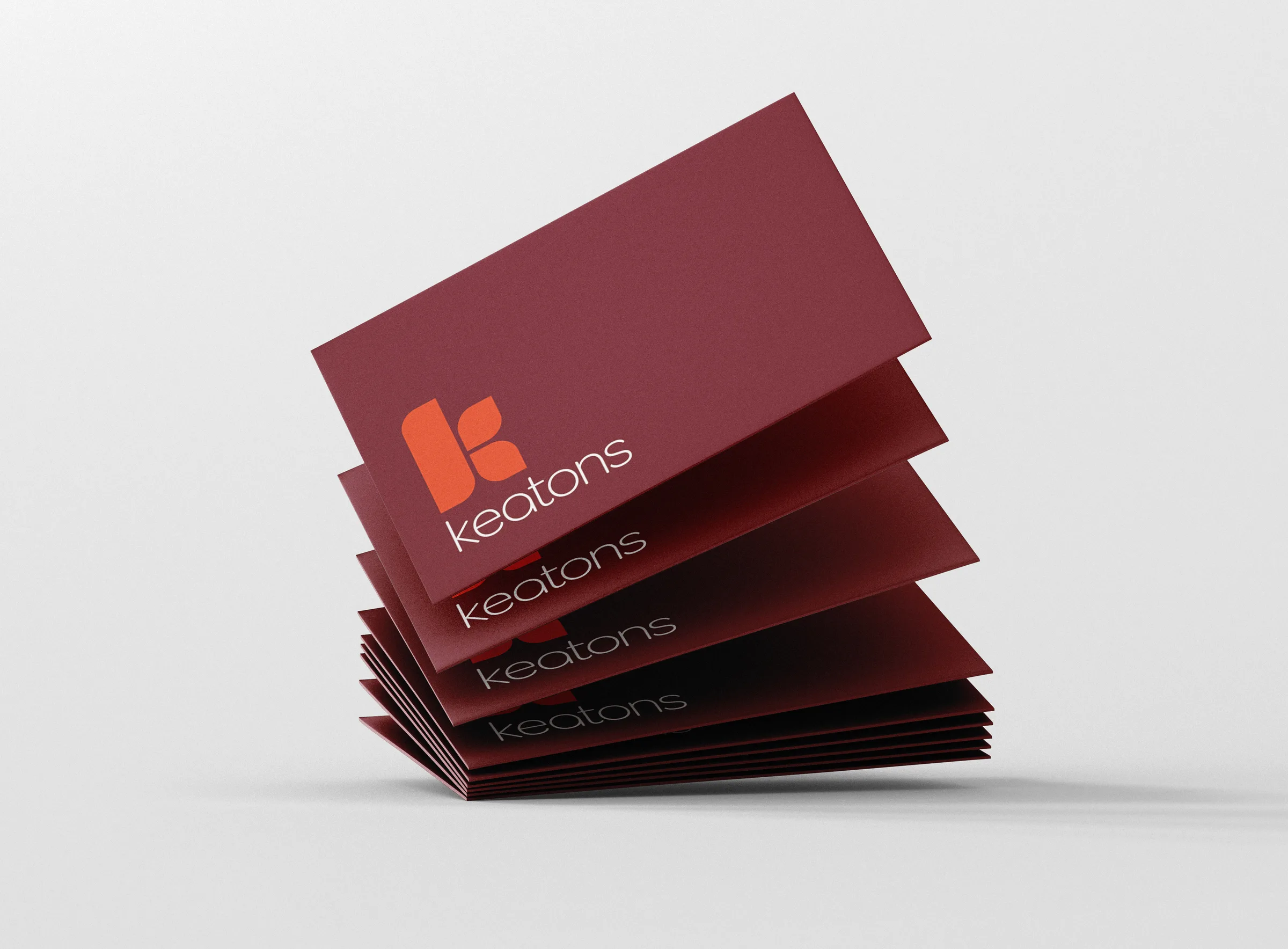 Burgundy Keatons business cards fanning out as they fall, each printed with the orange mark and white wordmark