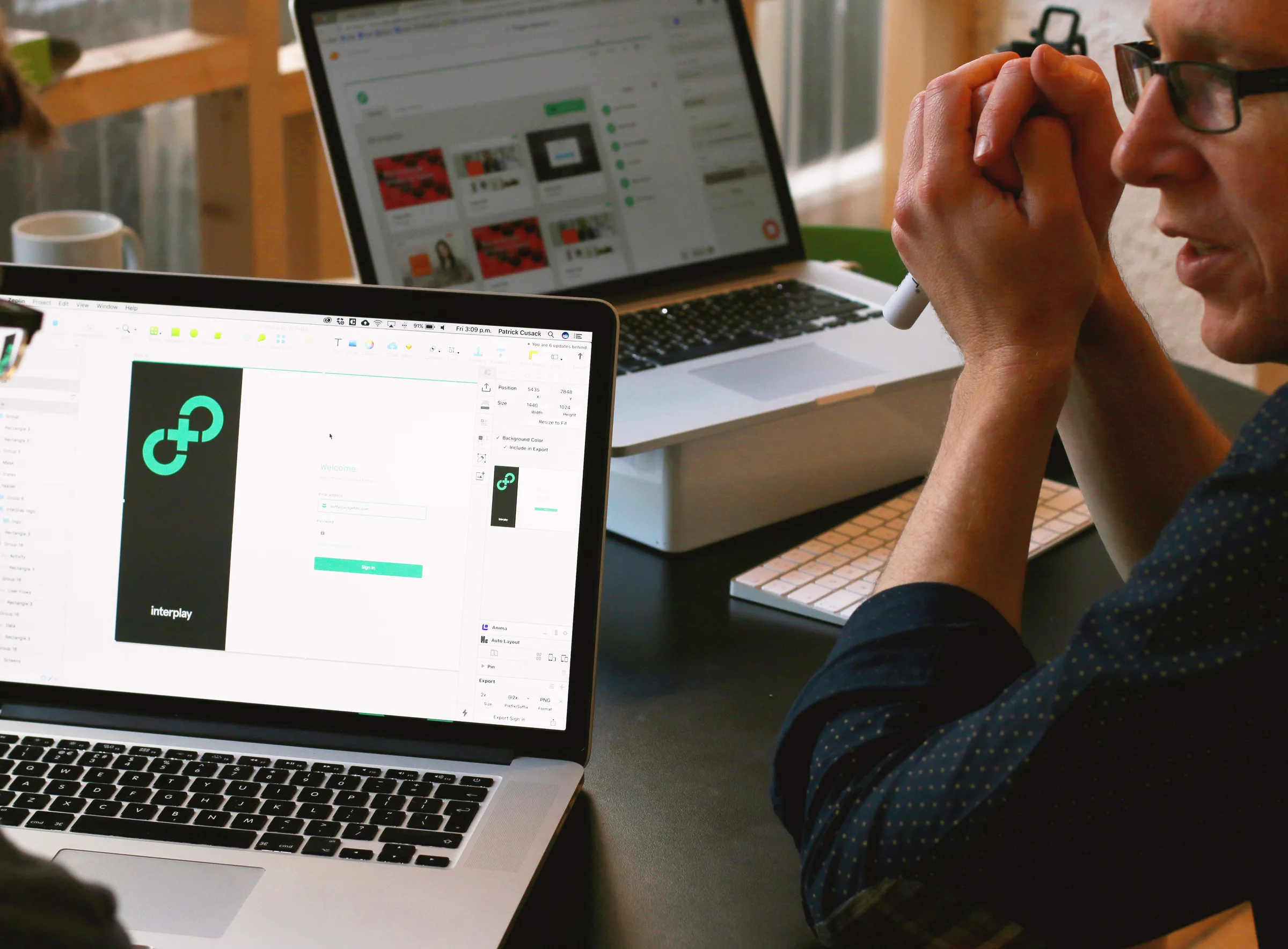 A design review with a laptop showing the Interplay sign-in screen in Sketch while a colleague looks on