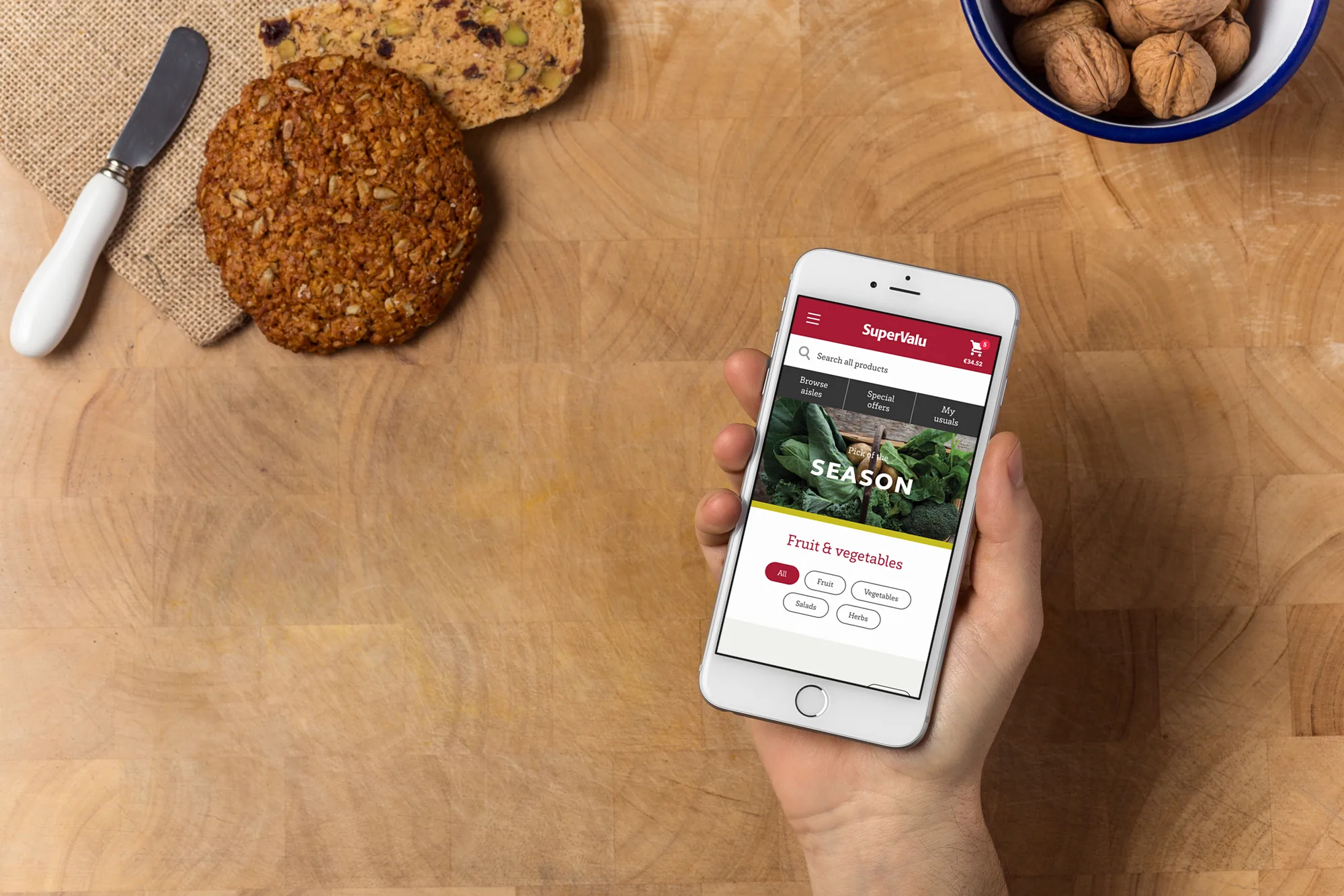 A hand holding a phone showing the Fruit & vegetables page above a wooden table