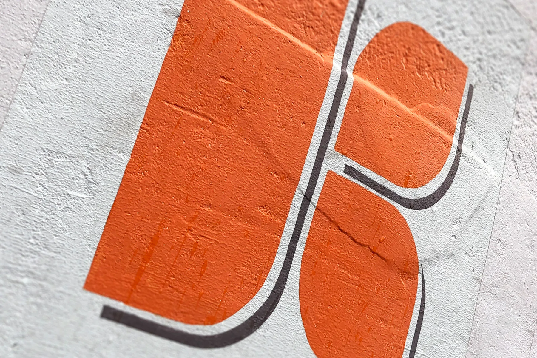 The Keatons K painted in orange with a dark drop line on a textured white wall