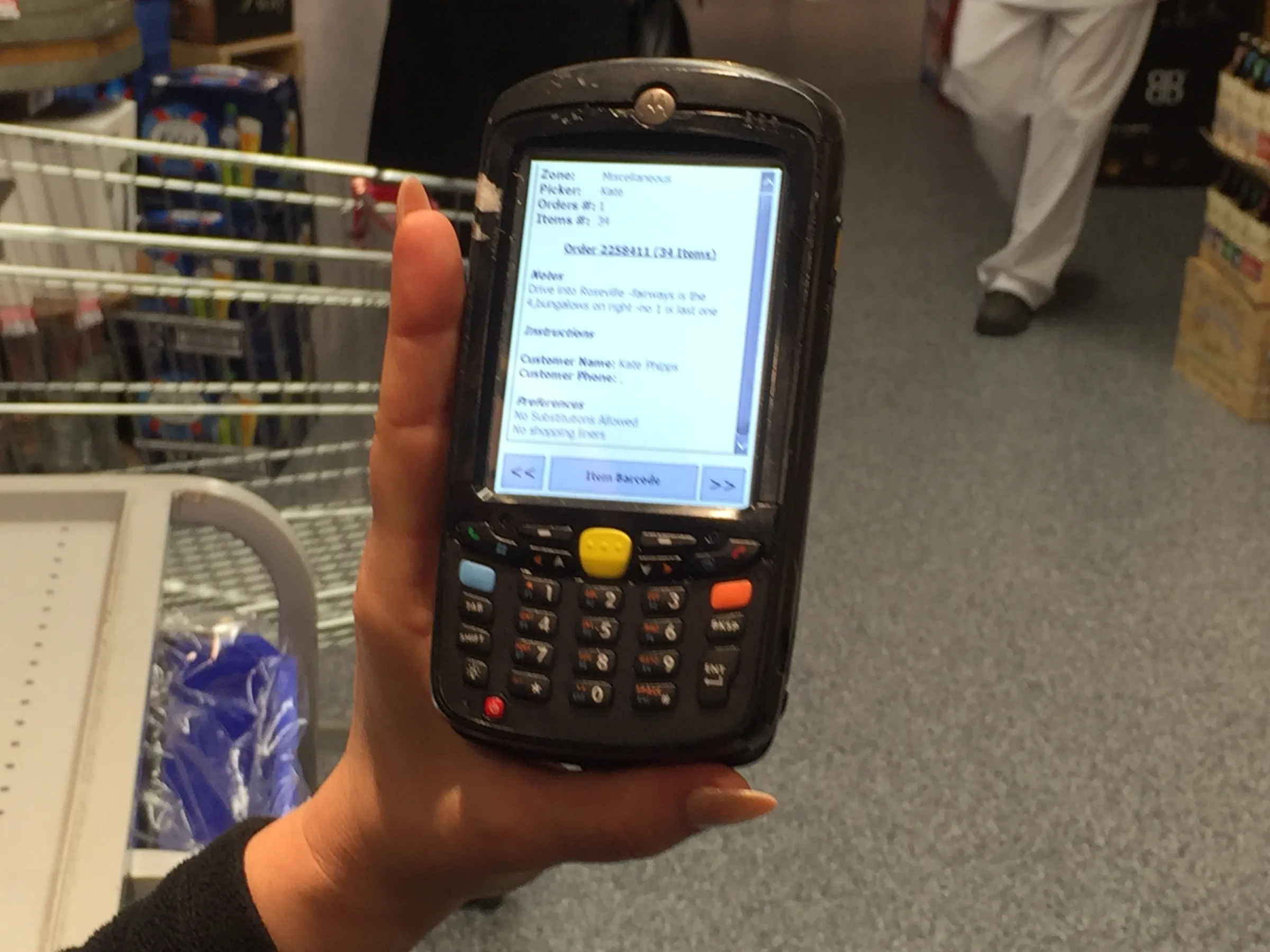 A hand holding a handheld scanner showing an order picking list
