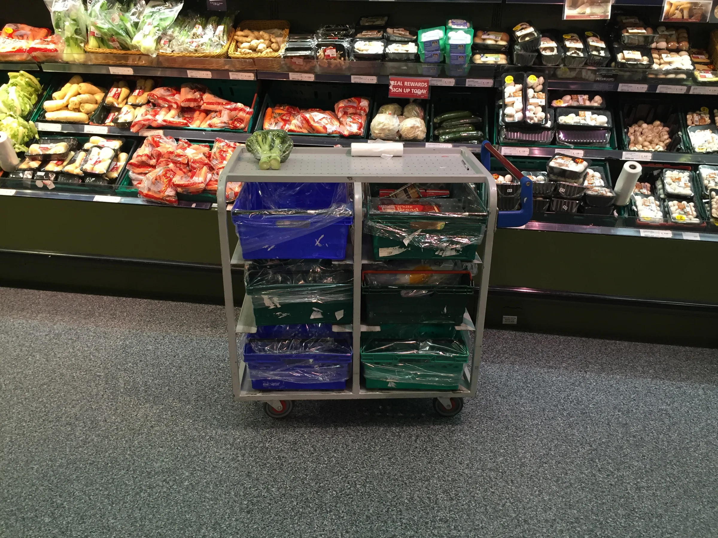 A picking trolley with green and blue crates in a supermarket aisle