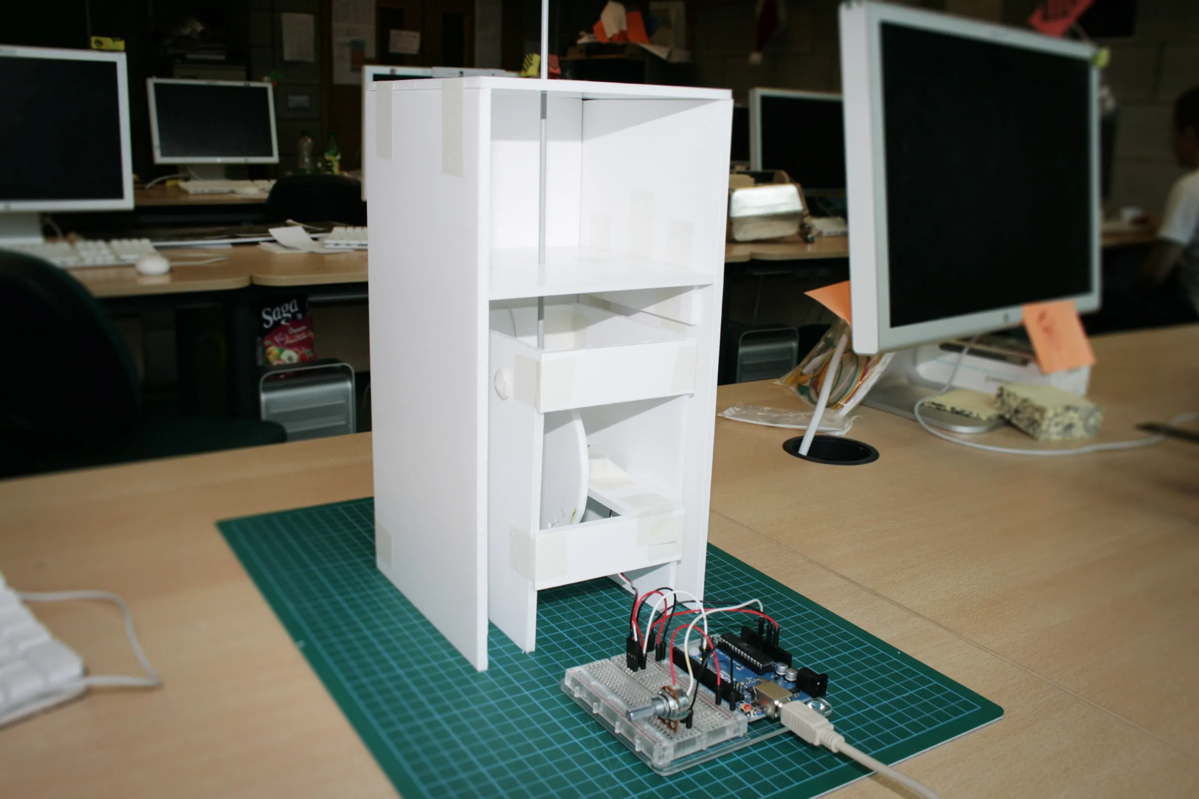 White foamboard prototype cabinet on a cutting mat, with a breadboard and Arduino wired to it at the base