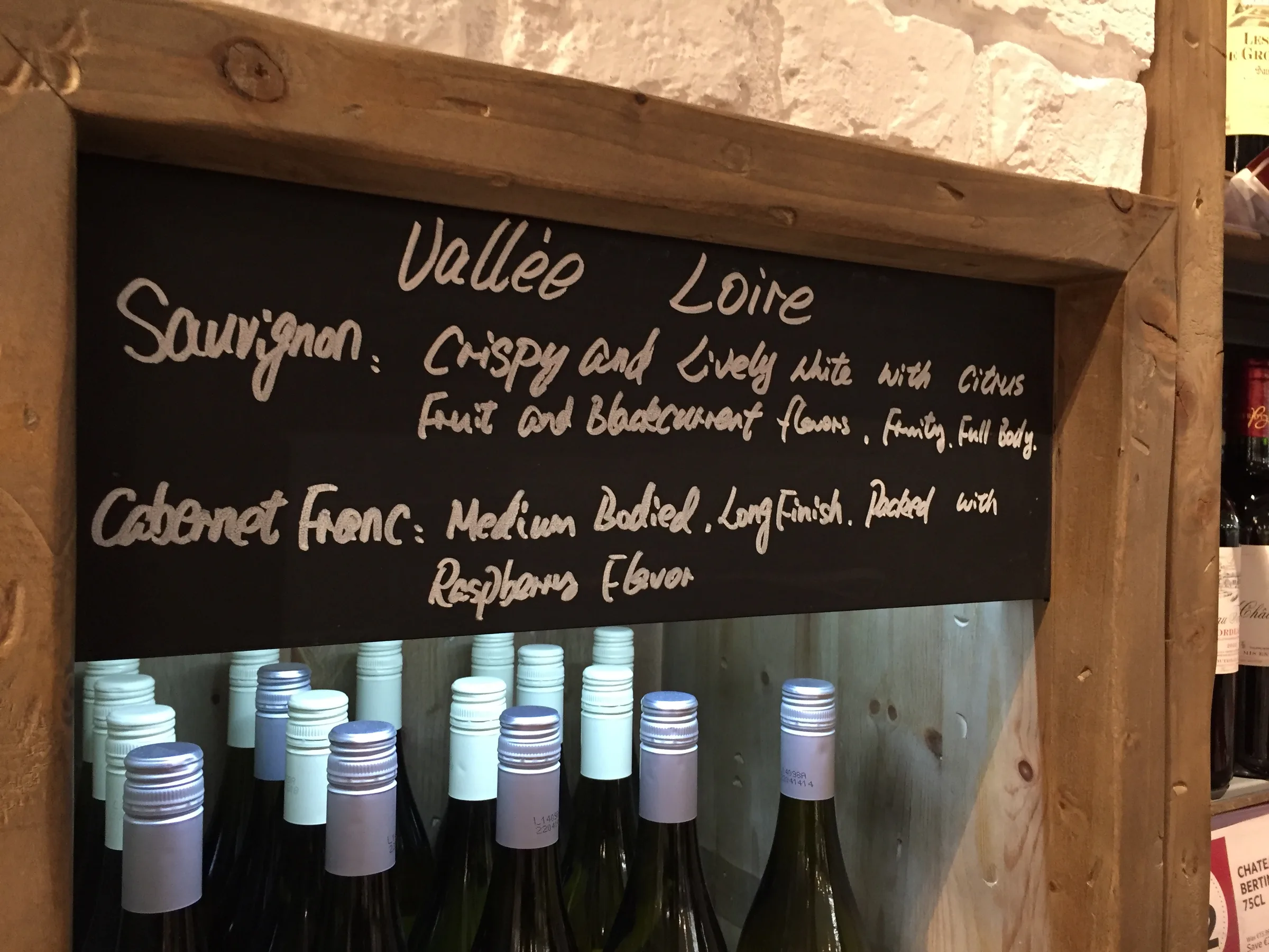 A chalkboard above a wine shelf with handwritten tasting notes for each grape