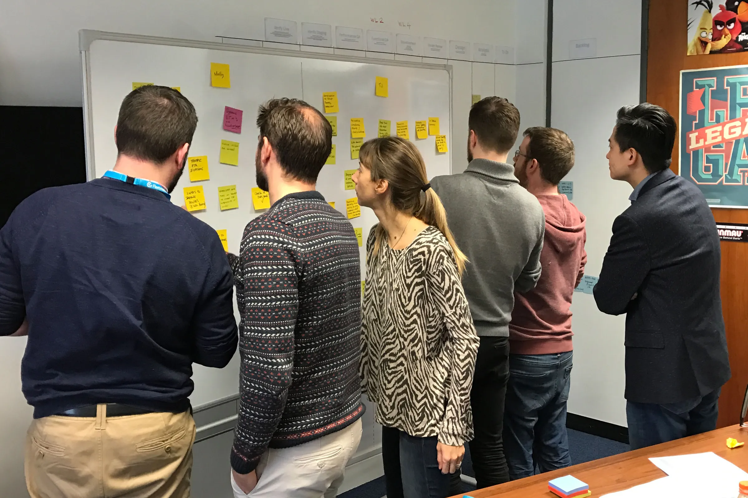 Six team members standing at a whiteboard covered in yellow sticky notes during a workshop
