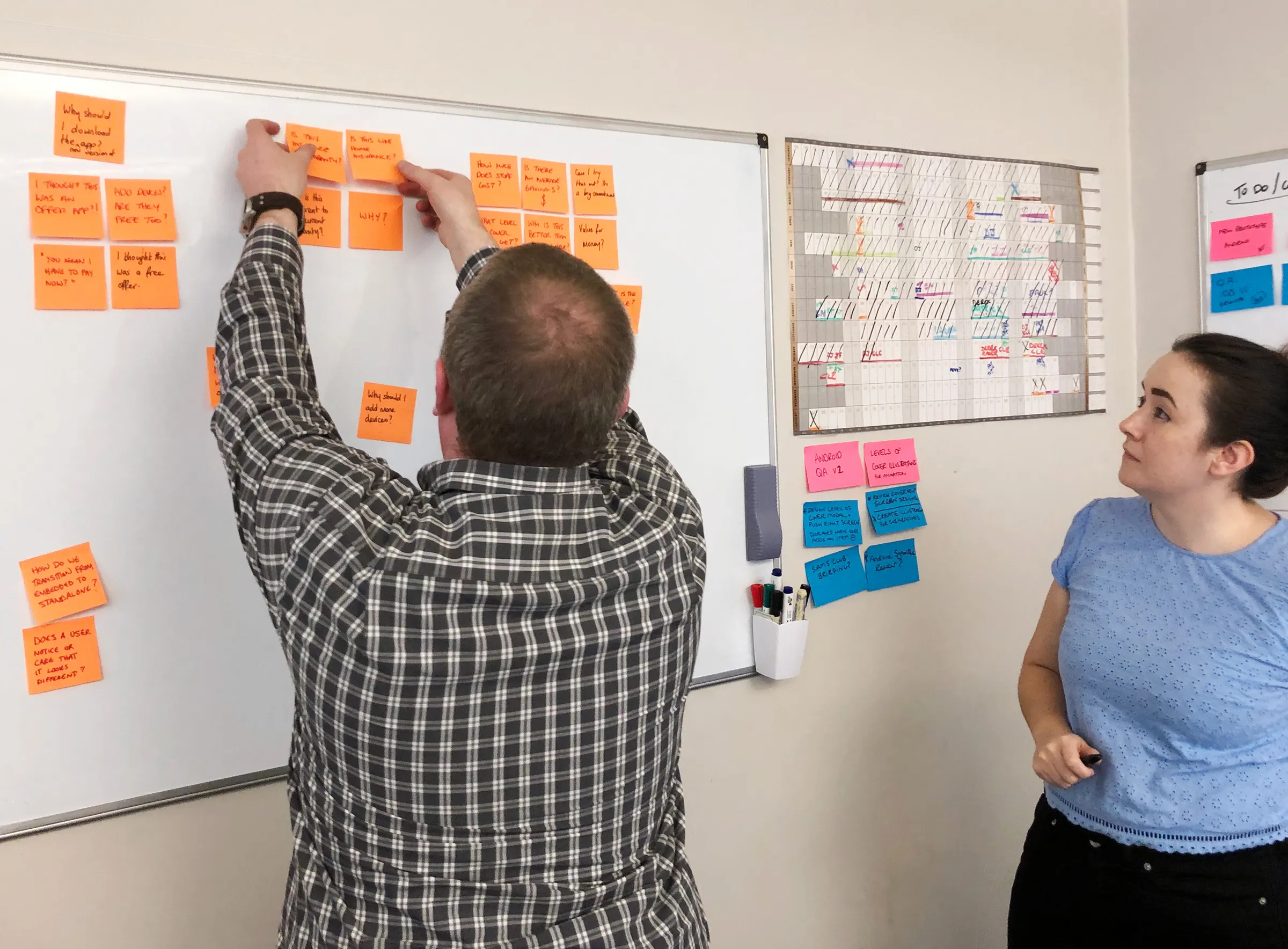Two team members arranging orange sticky notes of customer questions on a whiteboard